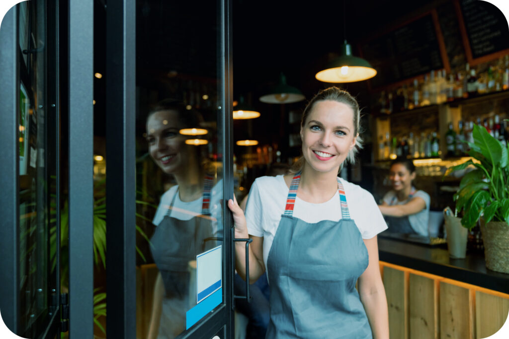 A smiling woman leaning holding bar door open